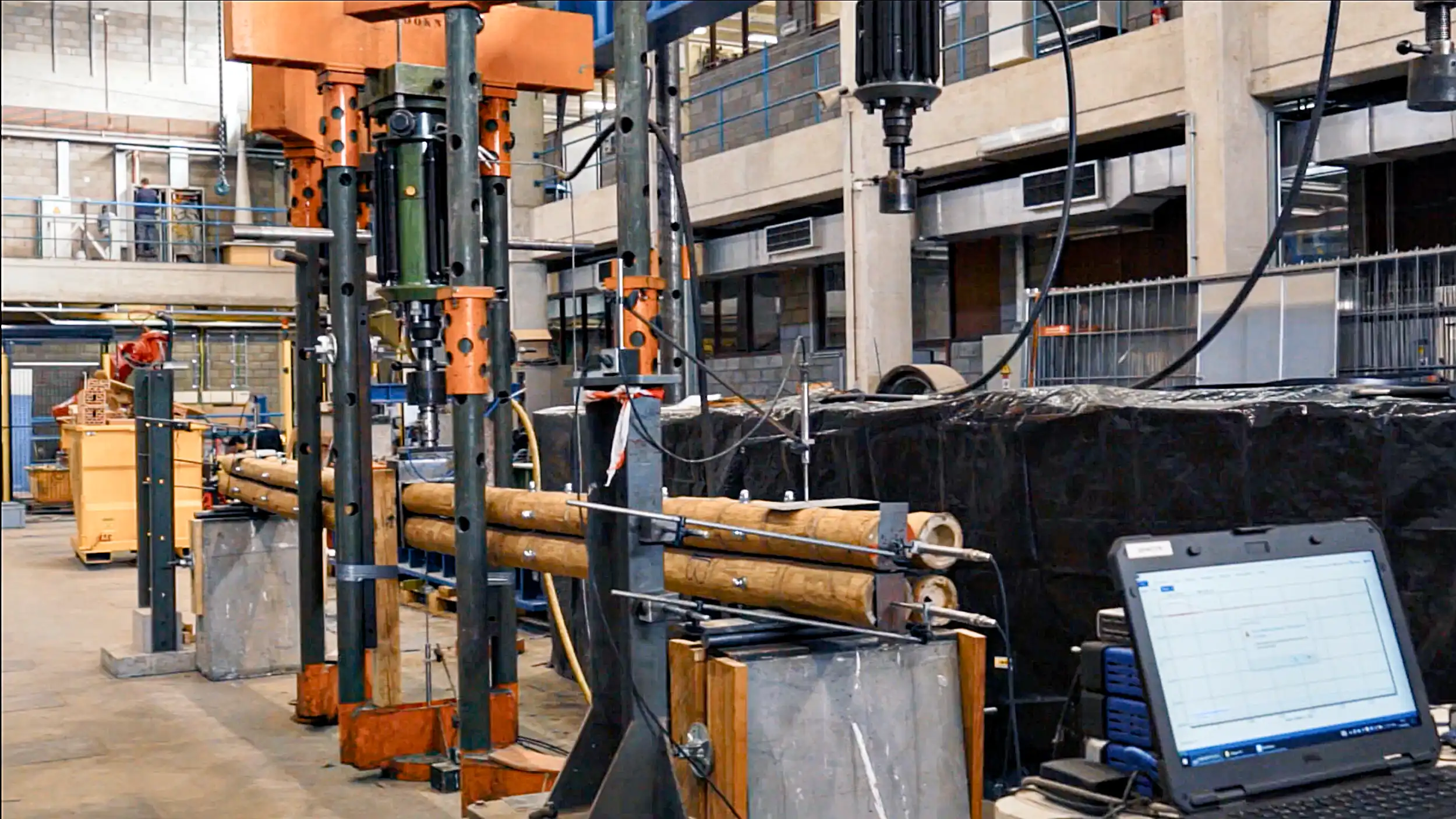 Structural Guadua bamboo poles undergoing laboratory flexural strength testing with digital load monitoring for NSR-10 engineering standards